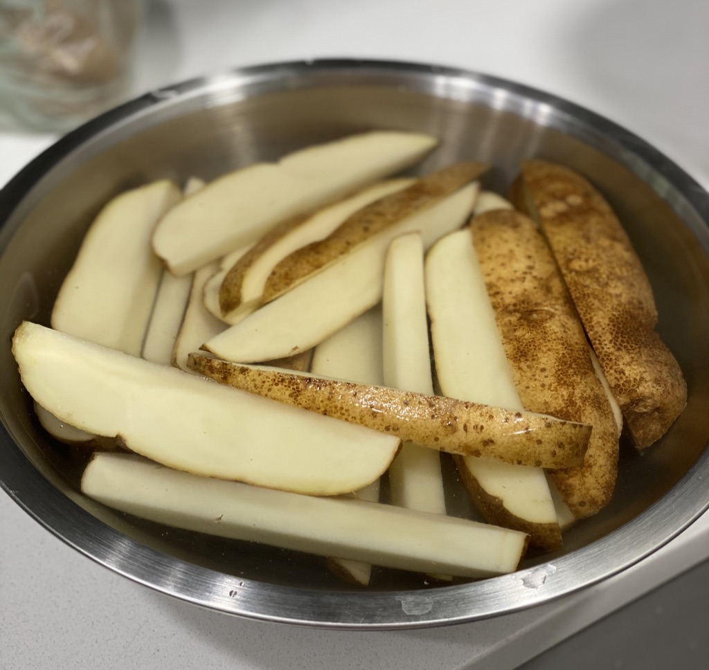 sliced potato wedges in bowl of water