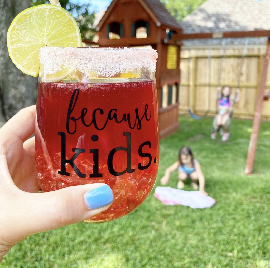 mom holding cocktail with kids playing in background