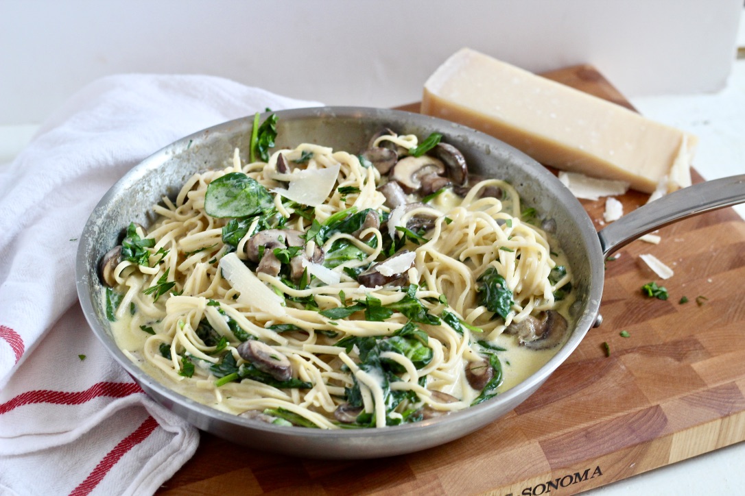 truffle mushroom pasta in stainless steel skillet on wood cutting board with parmesan cheese block