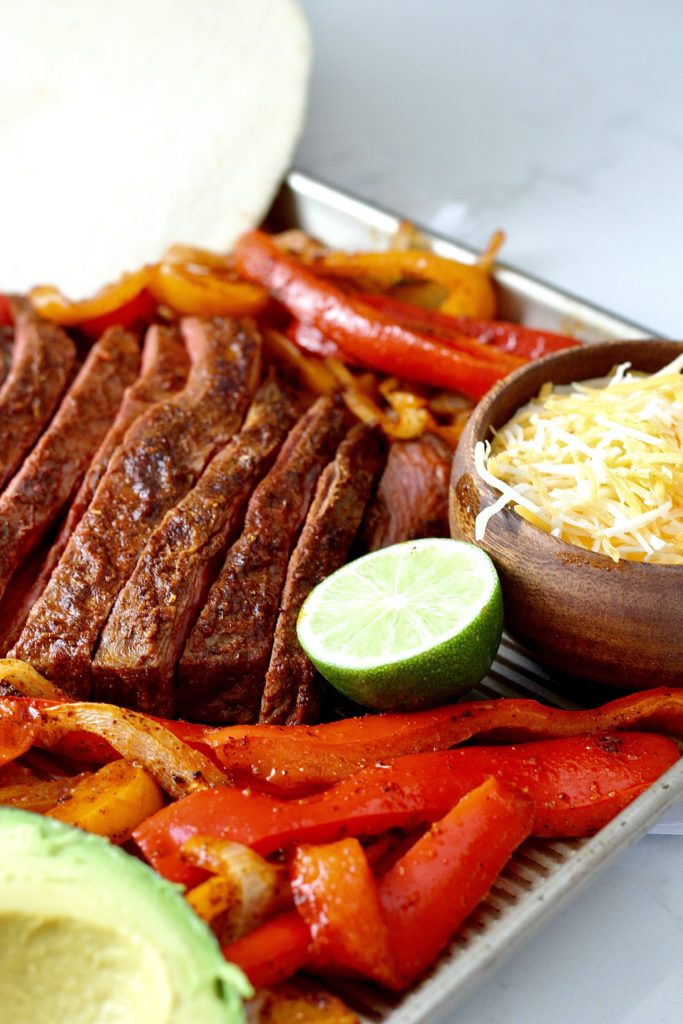 beef fajitas with shredded cheese on sheet pan